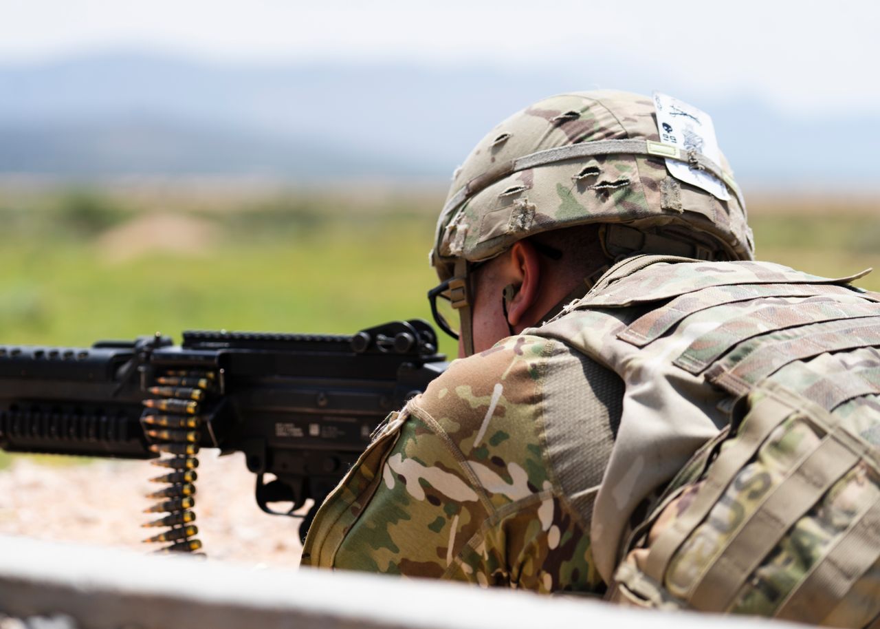 A soldier in camouflage aims with an automatic weapon in outdoor military training.